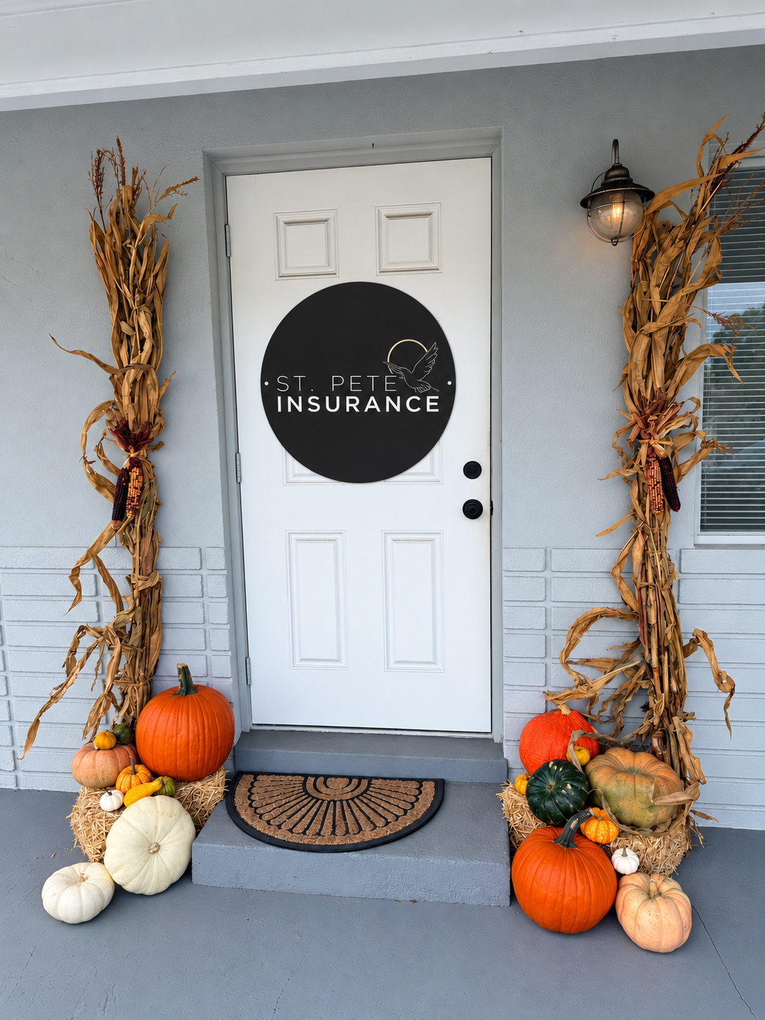 Residential porch styled with tall cornstalks flanking the front door and pumpkins on hay bales